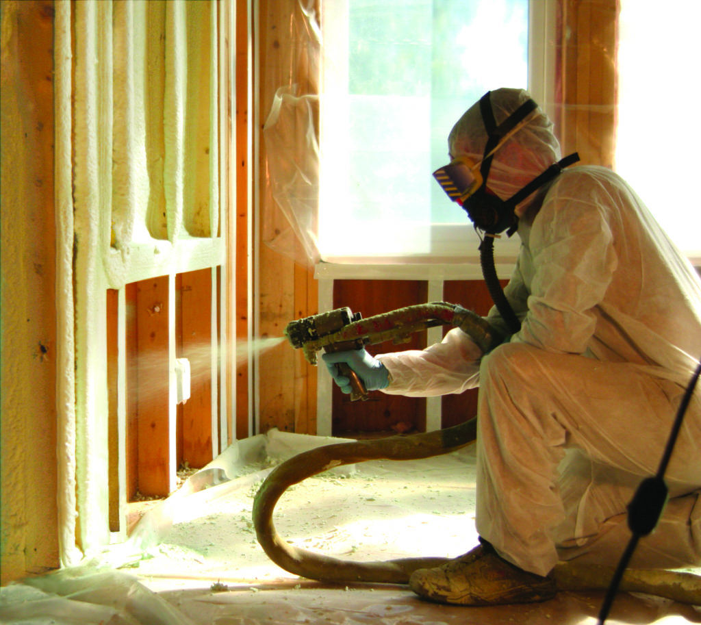 spray foam insulation being installed in a wall by technician wearing hazmat suit